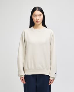 A light beige adult crew sweatshirt, featuring long sleeves and a subtle logo, displayed on a model.