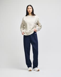 A model wears a beige Champion Reverse Weave® adult crew sweatshirt paired with navy trousers. The sweatshirt has a small logo.