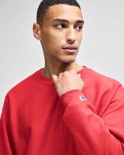 A red sweatshirt featuring a logo on the sleeve, modelled by a person looking to the side.