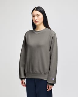 A grey Champion Reverse Weave® adult crew sweatshirt on a model, featuring a branding logo on the sleeve.