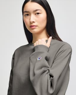 A grey Champion Reverse Weave® adult crew sweatshirt with a logo on the sleeve, modelled by a person.