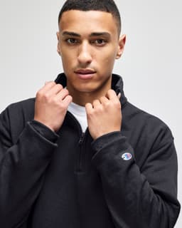 A man in a black quarter-zip pullover with a logo on the sleeve, posing against a neutral background.