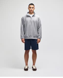 A grey quarter-zip pullover worn with navy shorts, featuring a logo on the sleeve.