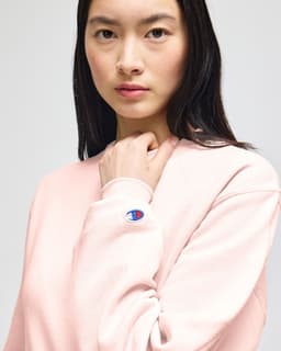 A cream-coloured crewneck sweatshirt with a logo on the sleeve, worn by a model.