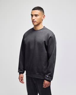A grey crewneck sweatshirt on a model, featuring a logo on the sleeve and a relaxed fit.