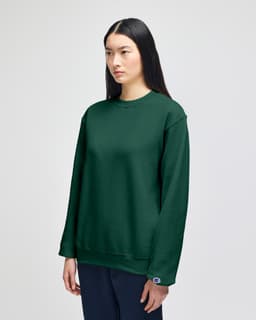 An olive green crewneck sweatshirt displayed on a model, featuring a logo on the sleeve.