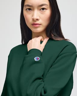A green crewneck sweatshirt displayed on a model, featuring a small logo on the arm.