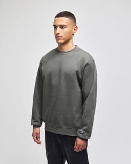 A green adult crewneck sweatshirt with a logo patch, featured on a model.