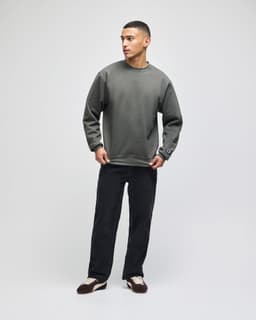 A grey adult crewneck sweatshirt with a pouch and branding, paired with dark pants.