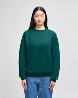 A green crewneck sweatshirt with a logo, displayed on a model wearing blue jeans.