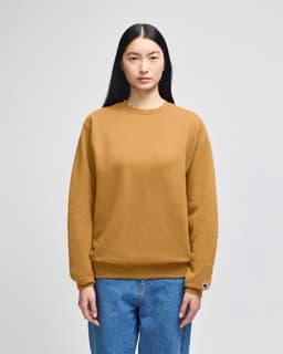 A model wears a mustard-coloured Champion Powerblend® crewneck sweatshirt, paired with blue jeans.
