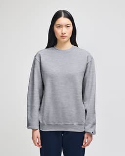 A grey Champion Powerblend® adult crewneck sweatshirt with a logo, featured on a model in casual attire.