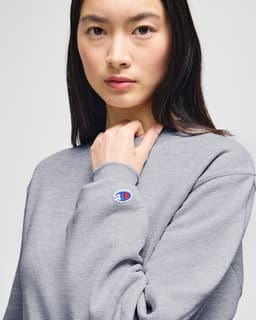 A grey crewneck sweatshirt on a model, featuring a logo on the sleeve. The fabric appears soft and comfortable.