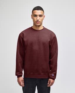 A maroon adult crewneck sweatshirt is worn by a model, featuring a subtle logo on the sleeve.