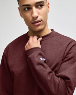 A maroon crewneck sweatshirt featuring long sleeves, with a logo on one sleeve.