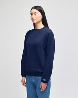 A navy blue crewneck sweatshirt displayed on a model, featuring a small logo on one sleeve.