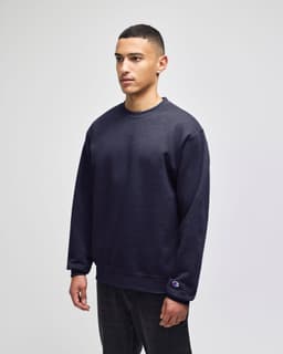 A dark navy crewneck sweatshirt on a model, featuring a logo on the sleeve and a relaxed fit.