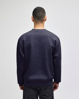 A navy crewneck sweatshirt displayed from the back, featuring long sleeves and a simple design. It has a logo.