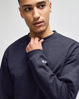 A navy crewneck sweatshirt worn by a male model, featuring a logo on the sleeve.