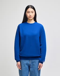 A vibrant blue crewneck sweatshirt is worn by a model, featuring a logo on the sleeve.