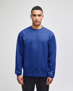 A blue crewneck sweatshirt is worn by a model, featuring a logo on the sleeve.