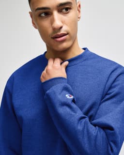 A blue crewneck sweatshirt on a model, featuring a logo on the sleeve.