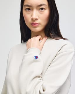 A lightweight, cream-coloured crewneck sweatshirt featuring a logo on the sleeve.
