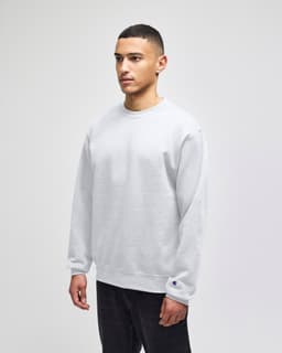 A grey crewneck sweatshirt on a model, featuring a small logo on the cuff.