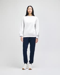 A model wearing a grey crewneck sweatshirt and navy tracksuit pants, standing against a plain background.
