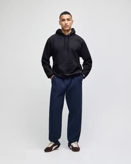 A black hooded sweatshirt paired with navy pants, featuring a logo on the sweatshirt.