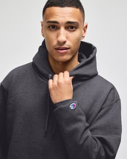 A dark grey pullover hooded sweatshirt on a model, featuring a logo on the sleeve.