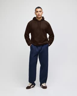 A brown hooded sweatshirt with a relaxed fit, paired with navy trousers and sneakers, featuring a logo.