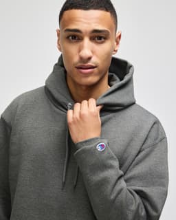 A grey pullover hooded sweatshirt on a model, featuring a logo on the sleeve.