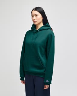 A green hooded sweatshirt with a front pocket and a logo on the sleeve, modelled by a woman.
