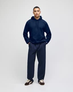 A navy blue pullover hooded sweatshirt on a model, paired with matching navy pants. The sweatshirt features a logo.