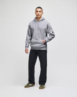 A man stands wearing a grey pullover hooded sweatshirt and navy shorts. The sweatshirt features a logo.