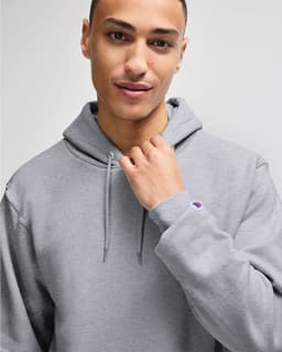 A grey hooded sweatshirt with a front pocket and a logo on the sleeve, modelled by a person.