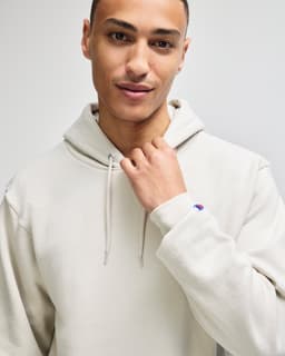 A light grey pullover hooded sweatshirt featuring a logo on the sleeve. Model wears it with a confident expression.