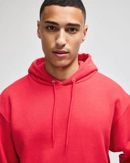 A red pullover hooded sweatshirt with a logo on the sleeve, worn by a model with a neutral expression.