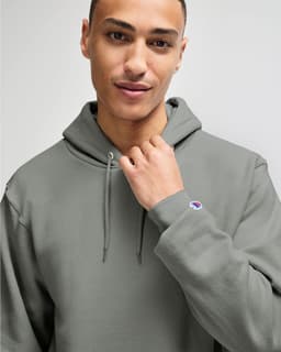 A grey hooded sweatshirt featuring a logo, with a male model wearing it and holding the hood.