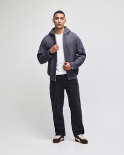 A model wearing a grey Champion Powerblend® full-zip hooded sweatshirt with a white shirt and black pants.