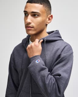 A grey full-zip hooded sweatshirt with a logo, worn by a young man looking to the side.