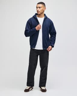 A man wearing a navy full-zip hooded sweatshirt paired with a white T-shirt and black pants.