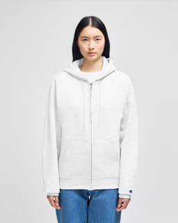A light grey full-zip hooded sweatshirt with a front pocket and a logo on the sleeve, worn by a model.