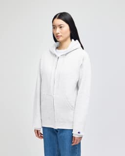 A grey full-zip hooded sweatshirt with a front pocket and a logo on the sleeve, displayed on a model.