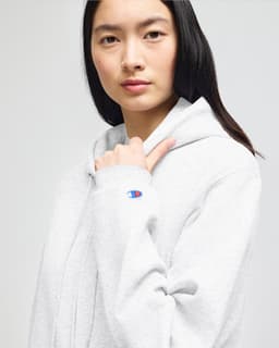 A grey full-zip hooded sweatshirt with a logo on the sleeve, featuring a model wearing it.