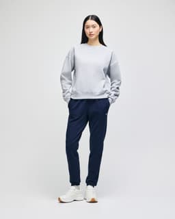 A grey women's crewneck sweatshirt paired with navy sweatpants and white sneakers, featuring a logo.