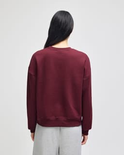 A maroon women's crewneck sweatshirt with a relaxed fit, featuring a branded logo on the back.