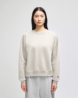 A light grey women's crewneck sweatshirt with a relaxed fit and a logo on one sleeve.