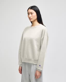 A light grey women's crewneck sweatshirt with a relaxed fit and a small logo on the sleeve.